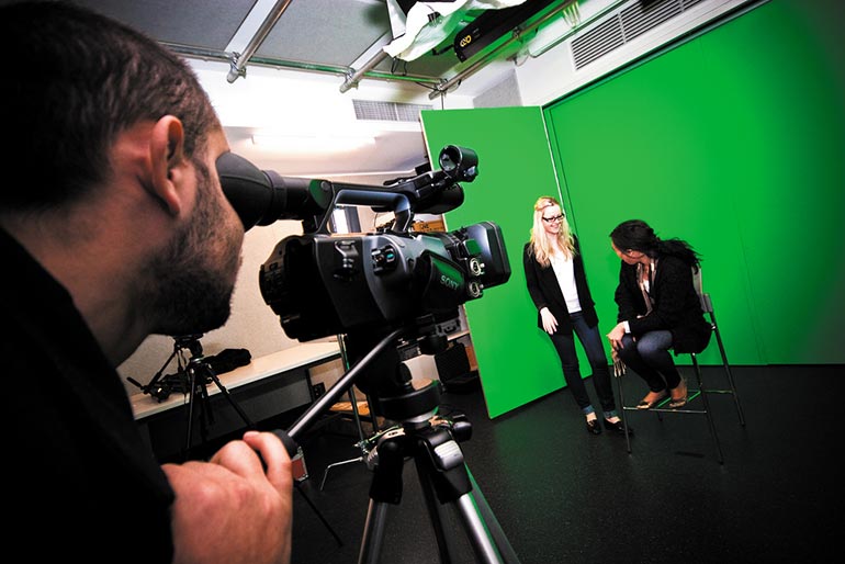 Two female students being filmed in front of a green screen.