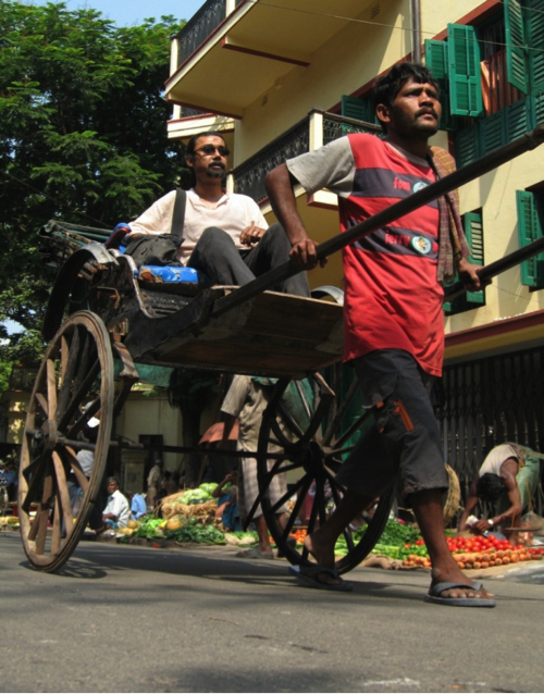 Man transports another man while walking a rickshaw.