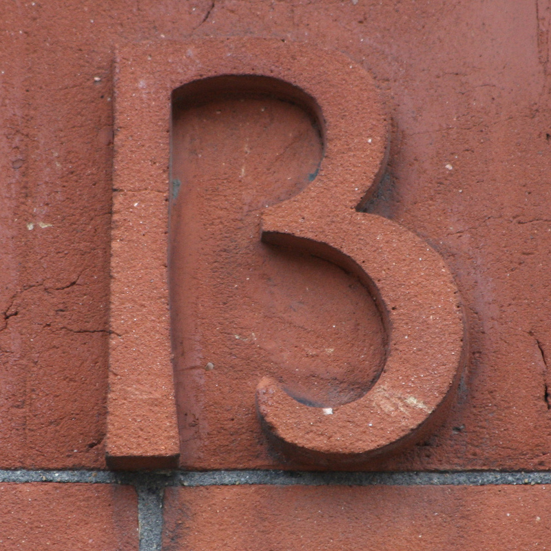 Close up image of the marking on the side of a building. It isn't clear if the marking is the number 13 or the letter B.