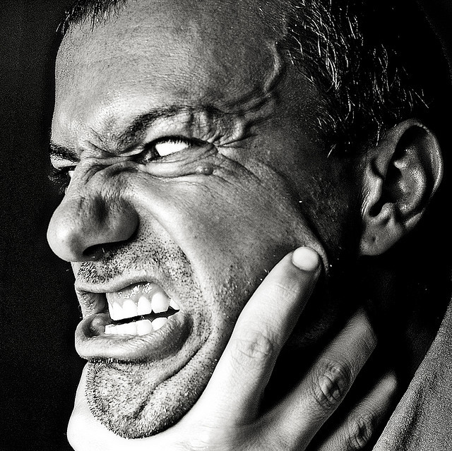 A man with an enraged look on his face and bulging veins on his forehead strains against a hand that is chocking him.