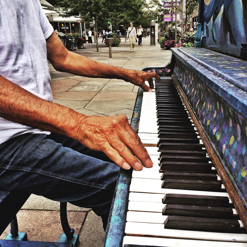 A man plays a piano on a sidewalk.