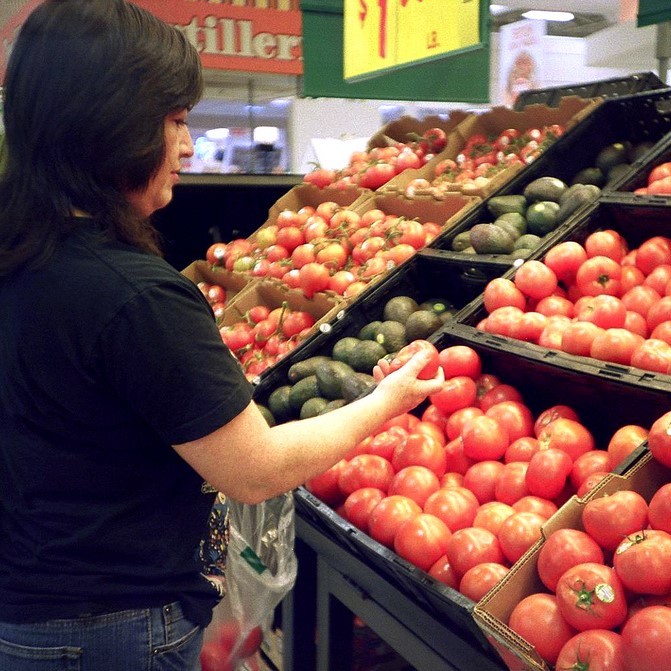 A woman inspects tomatoes as she puts them into a shopping bag.