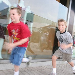 Two young boys sprint along the sidewalk.