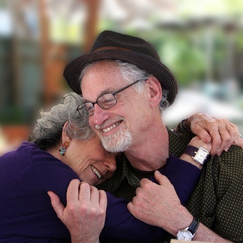 A grey-haired couple share an affectionate hug.