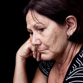 An older woman rests her head on her hand with a sad look on her face.