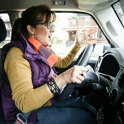 A woman shouts and makes an aggressive hand gesture as she drives her car.