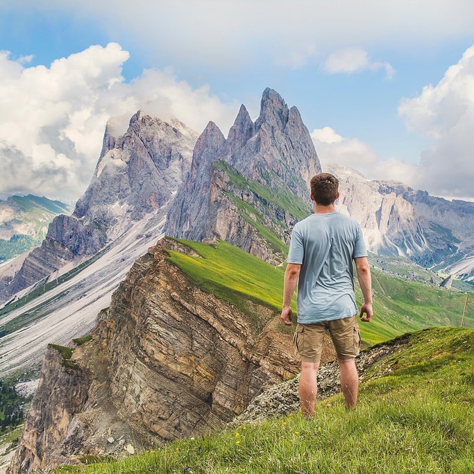 A man stands in an alpine meadow and looks into the distance at the high mountain peaks.