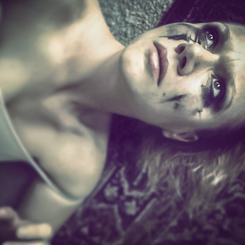 A distraught looking woman lies on the floor with makeup smeared across her face.