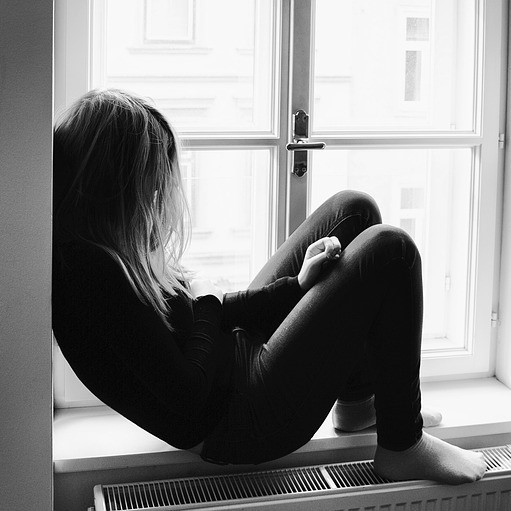 A young woman sits alone on a windowsill.