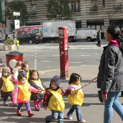 A group of preschool students are lead along a city street by an adult.