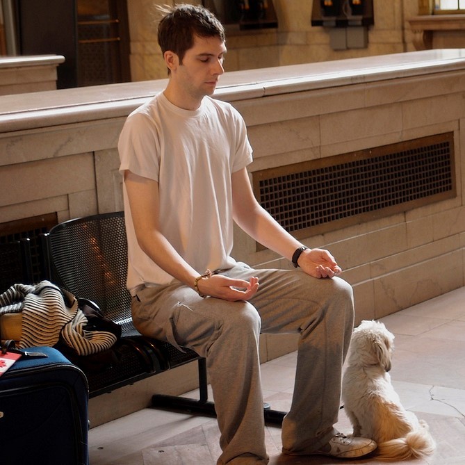 A young man meditates on a bench in a train station.