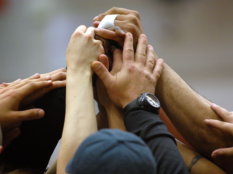 Members of a softball team put their hands together in the center of a circle to signify unity.