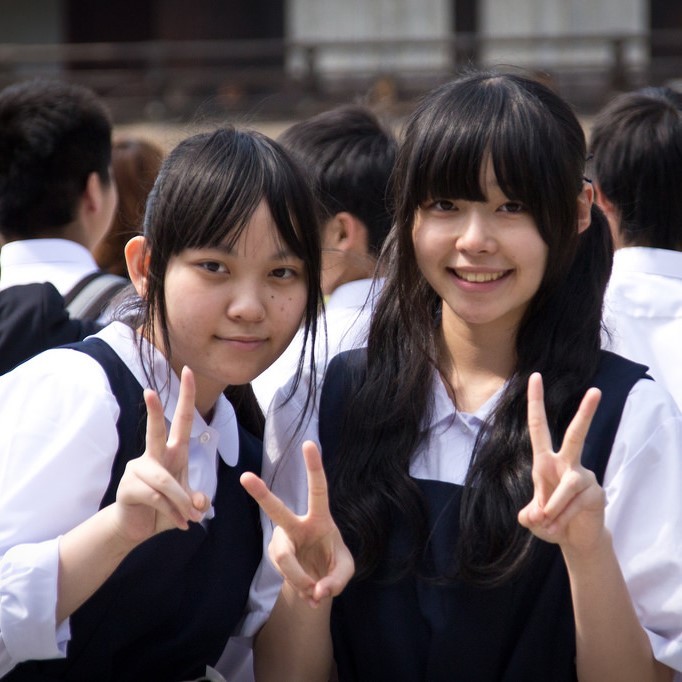Two Japanese school girls smile and flash a typical "V-sign" as the pose for a photo.