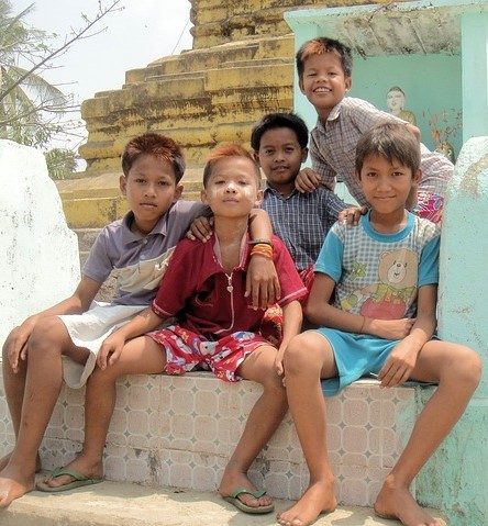 A group of young boys sit together on the steps with their arms around one another.