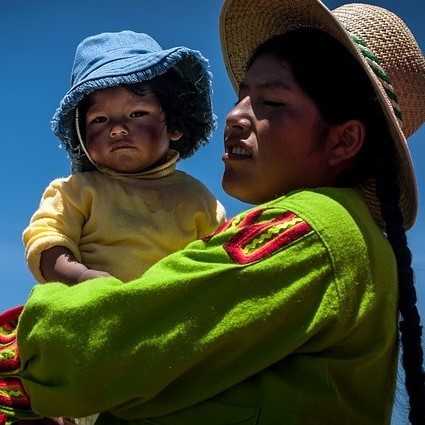 A woman dressed in traditional Bolivian clothes and hat holds her baby in her arms.