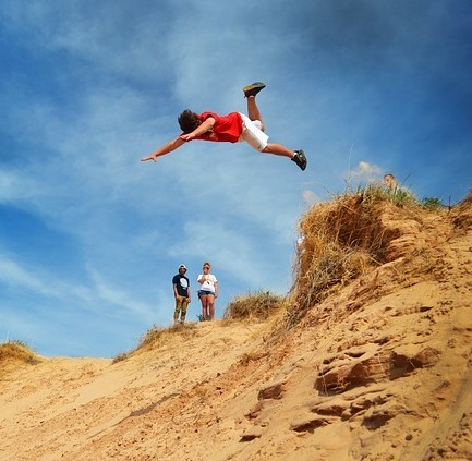 A young man jumps head first off the top of a sand dune and down a steep slope.