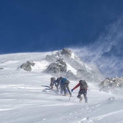 A group of mountaineers climbing to a snowy summit.