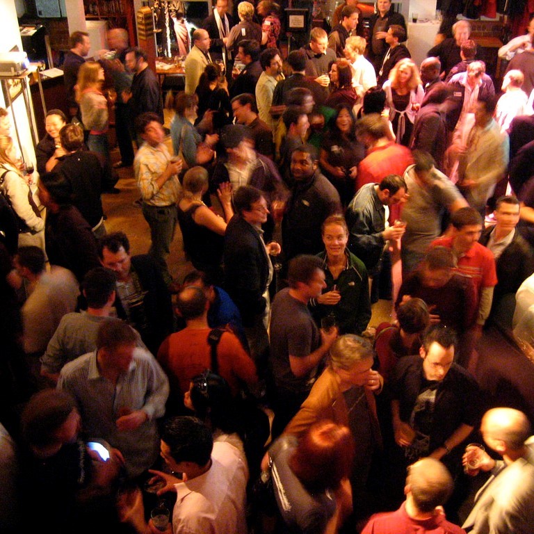 People stand and talk in groups of 3 or 4 during a party.