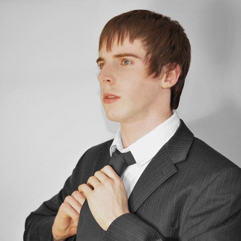 A young man in a suit adjusts his tie.