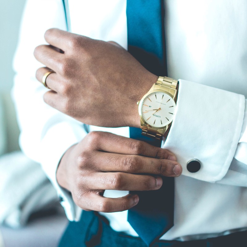 A man dressed in business attire and an expensive watch adjusts his cufflinks.