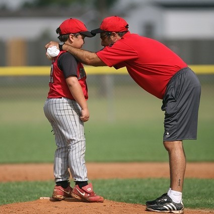 A baseball coach gives encouragement to a little league pitcher as they stand together on the mound.