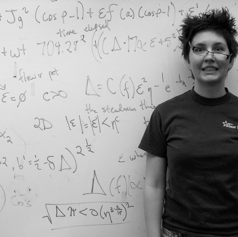 A woman stands triumphant but slightly disheveled after solving a complicated math problem on the whiteboard.