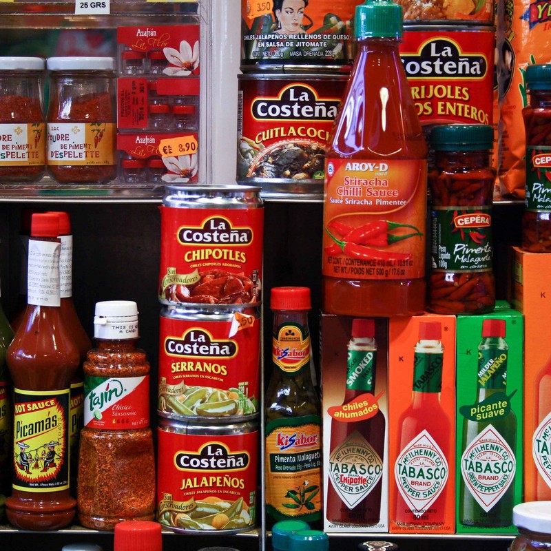 A selection of canned peppers and hot sauces on a supermarket shelf.