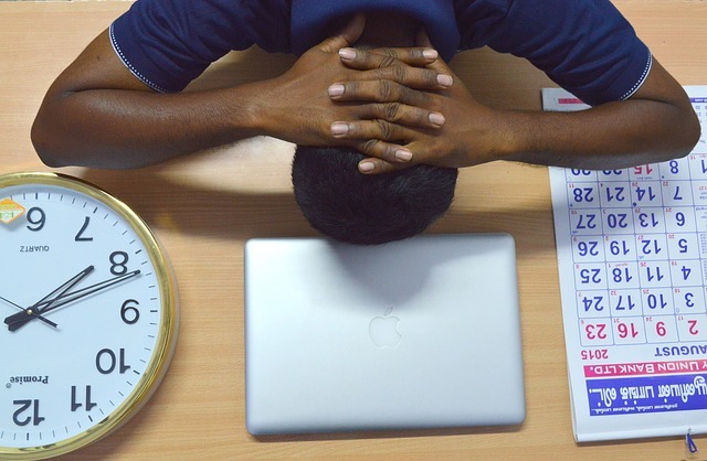 A student sitting between a clock and a calendar puts his head down on his desk in frustration.