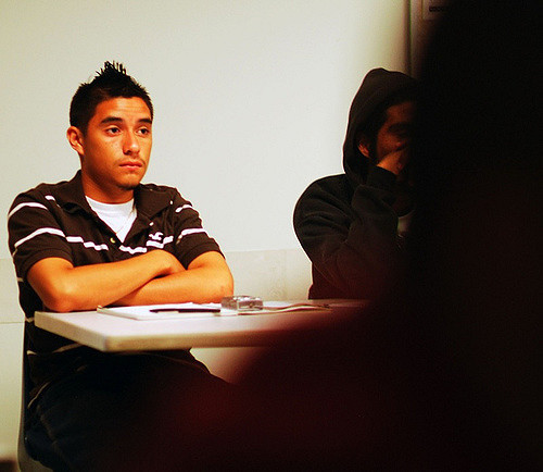 A student sits in the back of a classroom with his arms folded and a blank stare on his face.
