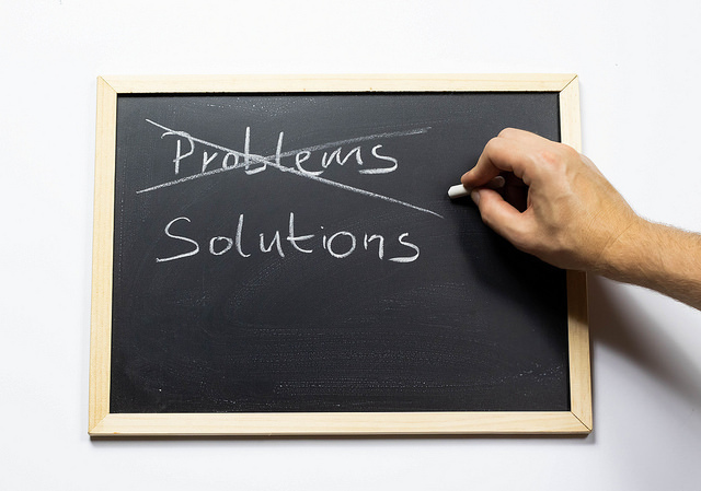 Person crossing out the word “Problems” and replacing it with a word “Solutions” in chalk on a blackboard.