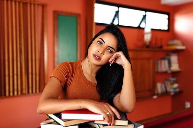 A young woman resting her head on her arm which rests of an a pile of books