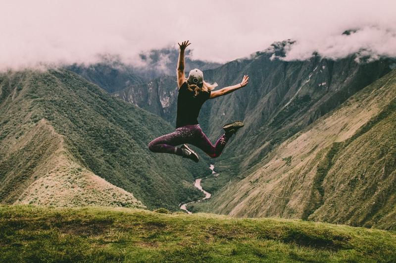 A person jumping up with hands and feet in the air on a mountaintop