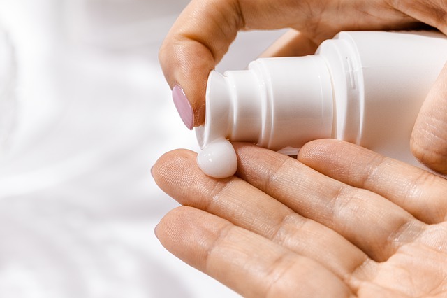 A person squeezing a dollop of hand lotion on their fingers from a lotion bottle 