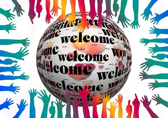 A sphere with the word "welcome" written on it many times and hands of different colors outstretched towards it from the edges of the image