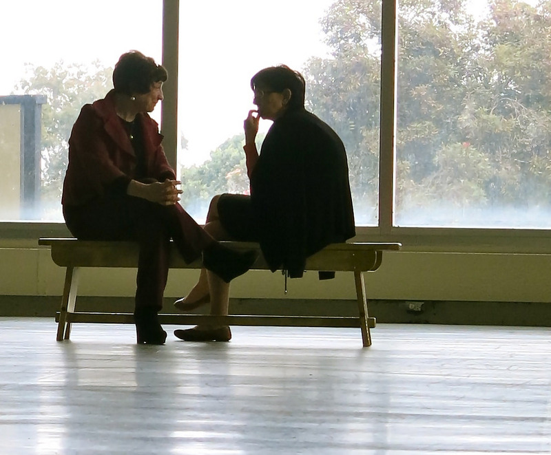 Two women sit having a quiet conversation in a public place.