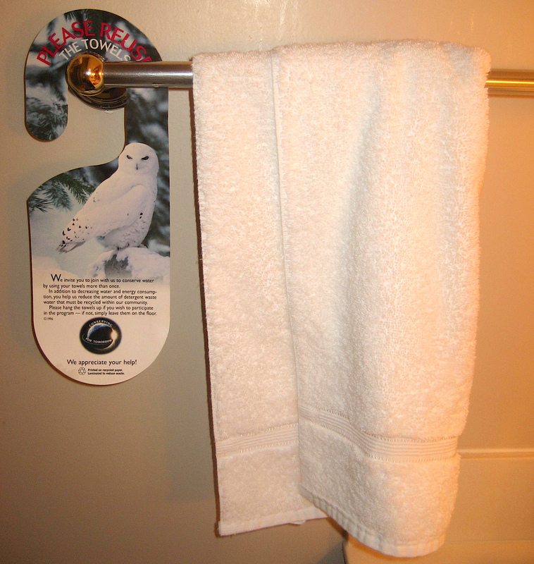 A towel rack in a hotel guest bathroom has a white towel hanging next to an informational sign about how to save water.
