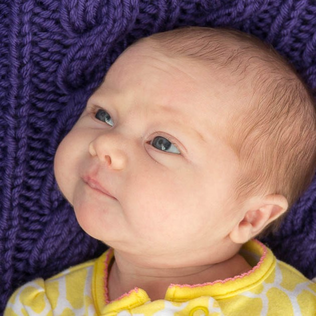 An infant lies on its back with its eyes fixed on a nearby object.