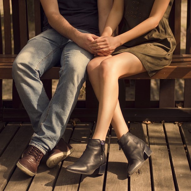 A couple holding hands on a bench.