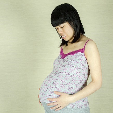 A pregnant woman smiles as she looks down at her belly.