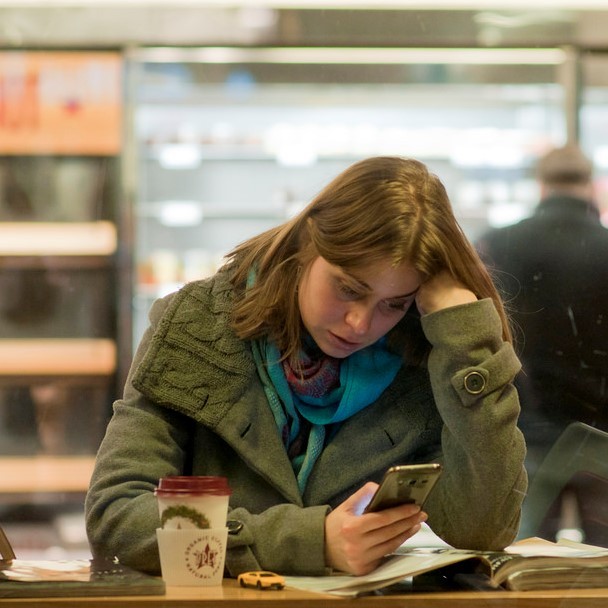 A woman sits at the counter of a coffee shop while using her smartphone.