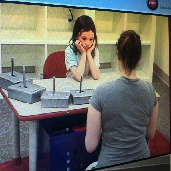 An experimenter sits at a table across from a young girl who is a participant in a laboratory experiment.