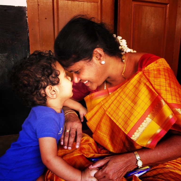 A mother smiles broadly as she nuzzle noses with her toddler son.