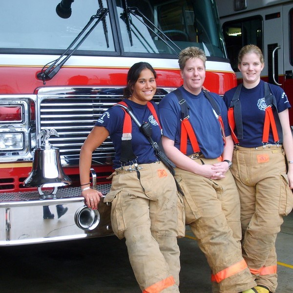 Three female members of a fire and rescue team stand in front of a fire engine wearing firefighting safety clothing.