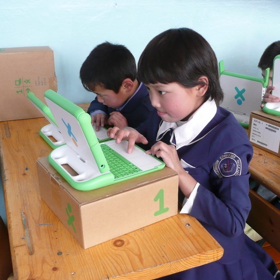 Una joven colegiala de uniforme se sienta en su escritorio trabajando con atención en una computadora portátil.