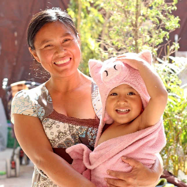 A smiling mother holds her happy toddler in a towel after a bath.