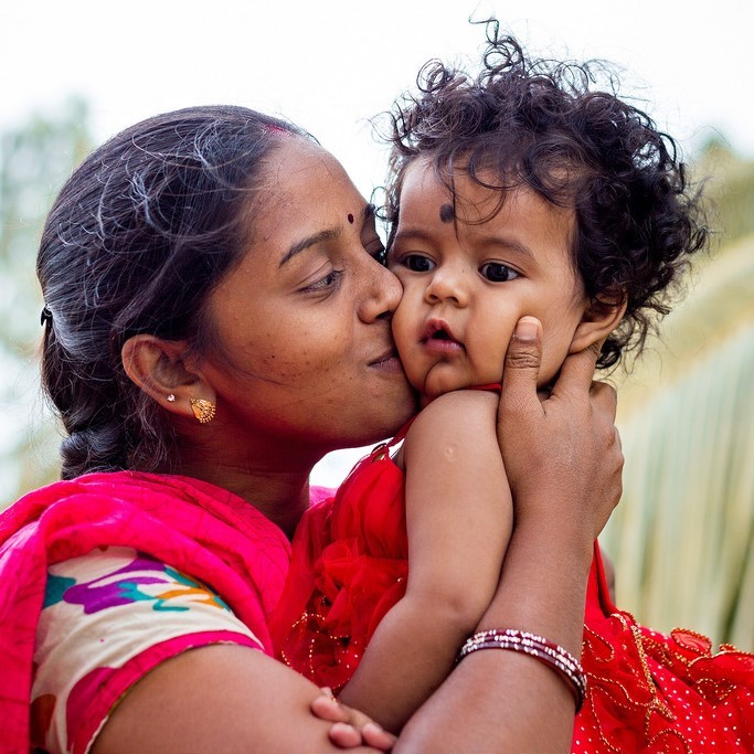 A mother looks lovingly at her son as she holds him in her arms and kisses him on the cheek.