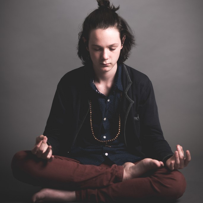 A young man sits in the lotus position meditating.