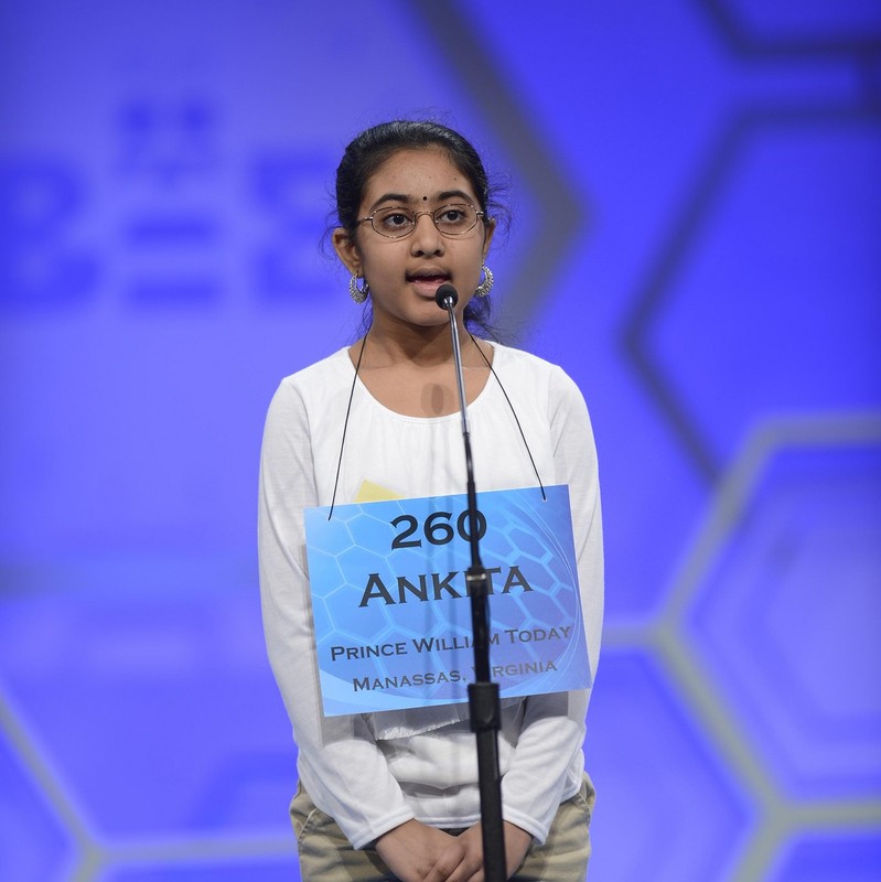 Una niña se para en el escenario frente a un micrófono mientras intenta deletrear una palabra en el Concurso Nacional de Ortografía de Scripps.