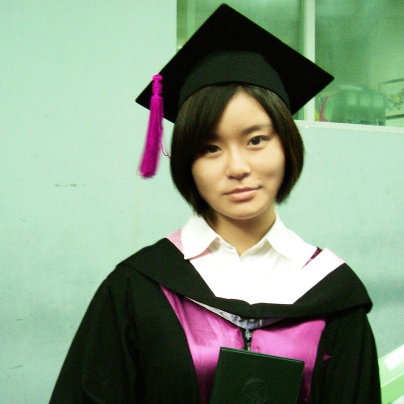 Una mujer del este de Asia vestida con una gorra y un vestido de graduación lleva una expresión neutra o tenaz.