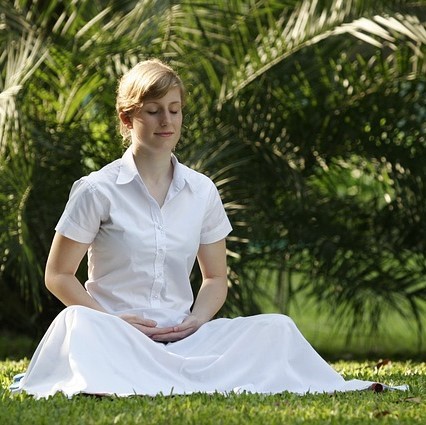 A woman sits in the grass meditating.
